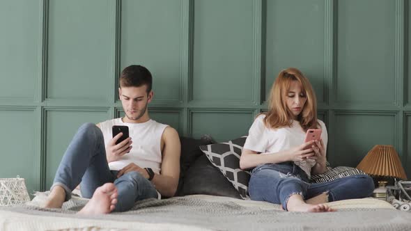 Young Couple Are Browsing Smartphones in Their Bed at Home alt
