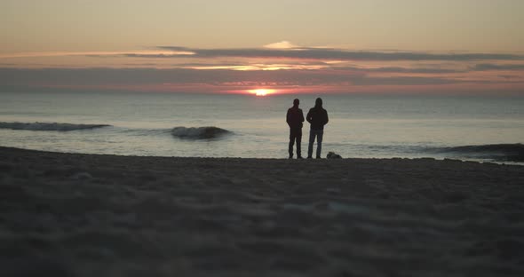Two friends standing on the beach and watch the sunset alt