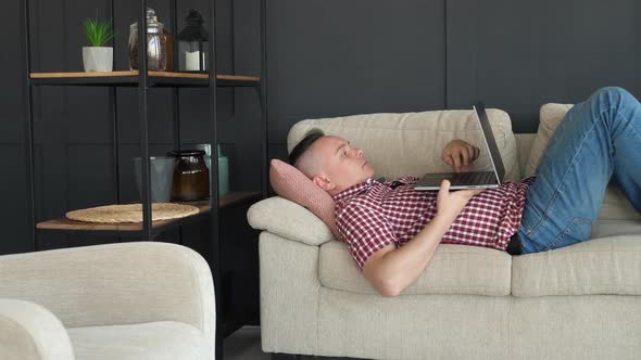 Freelancer Lies on Sofa and Types Text on Laptop