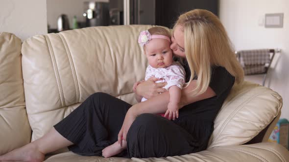 Mother Hugs and Kisses Her Adorable Baby on Sofa