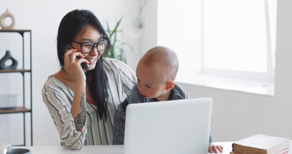 Young Mother Freelancer with Her Child Working at Home Office Using Laptop alt