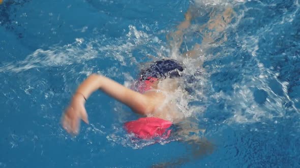 a Woman Swimmer in a Red Cap and a Swimsuit Swims Breaststroke in the Pool During a Swimming