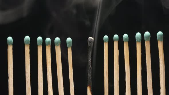 Smoke of single burned matchstick between row of new matchsticks