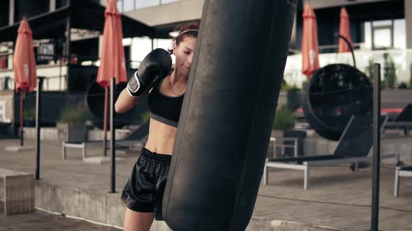 Attractive Athletic Female Boxer in Gloves Kicking a Punching Bag alt