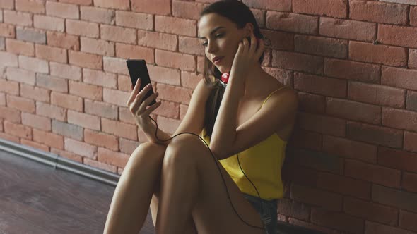 Attractive Young Female with Modern Headphones Browsing Smartphone and Listen To the Music alt