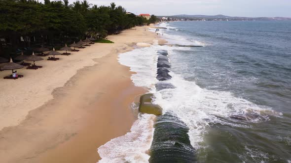 Man made geo tube protecting sandy beach from strong ocean waves, aerial fly over shot alt