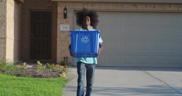 African American adolescents with huge Afro smiling as he hold recycle bin full of plastic bottles alt