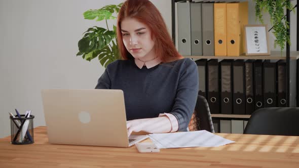 Young professional red hair female student using computer sitting at office desk. Focused business w