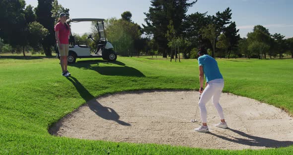 Two caucasian women playing golf wearing face masks one taking shot from bunker alt
