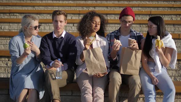 Group of Hungry Students Having Lunch Sitting on Stairs alt