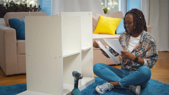 Young African Woman with Screwdriver and Instruction Assembling New Cupboard at Home alt