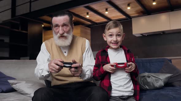 Bearded Man and His Teen Grandson which Having Fun Together at Playing Video Games  alt
