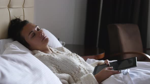 Young Pretty Woman Works with a Tablet While Lying in Bed and Falls Asleep Holding the Tablet
