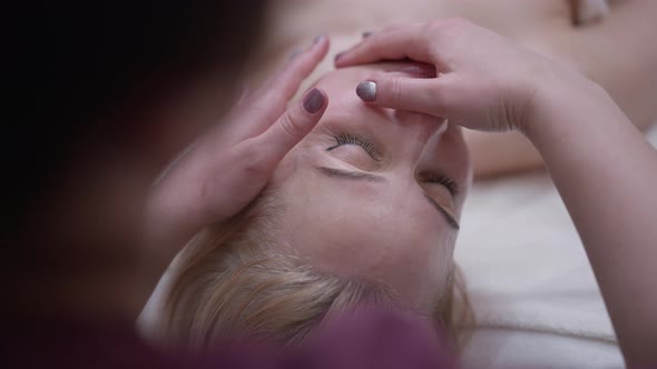 Shooting Over Shoulder of Professional Masseur Massaging Facial Skin in Slow Motion alt