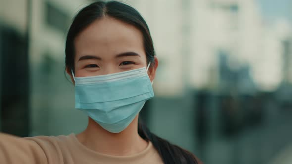 OV shot of Young Pretty Asian Woman in medical protective mask having a video call