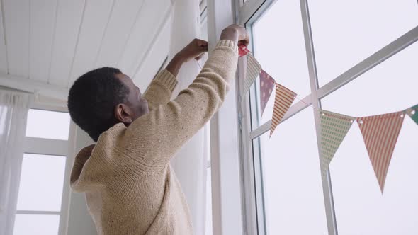 African American Man Hangs Colorful Pennant Banners in Room alt