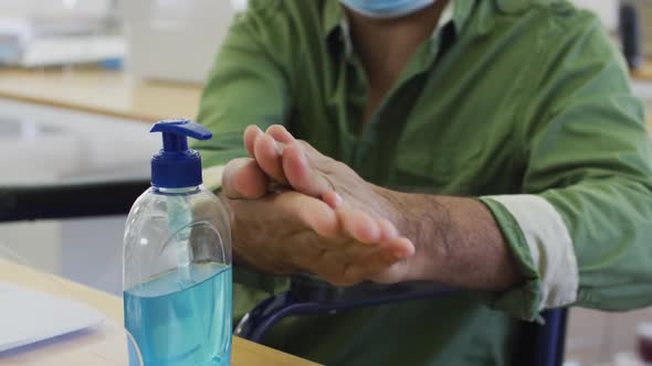 Man wearing face mask sanitizing his hands at office alt
