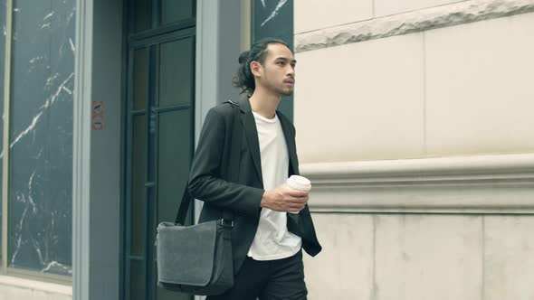 Young Asian businessman casual dress holding coffee cup during walking in the street.