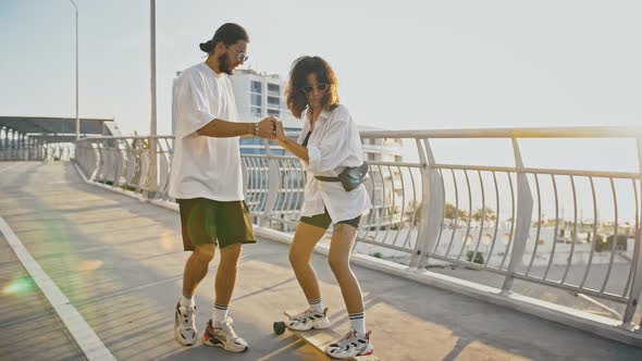 Young Man Teaching His Girlfriend to Skateboard Help Her to Ride alt