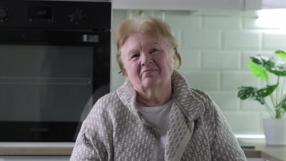 Head And Shoulders Portrait of Happy Senior Woman Sitting in Kitchen at Home alt