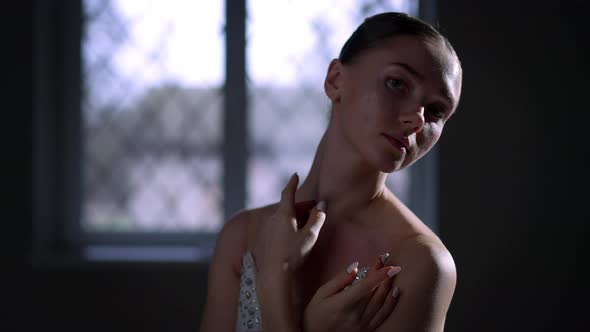 Charming Ballerina in White Dress Looking at Camera Standing in Darkness Indoors alt