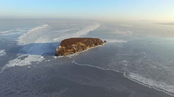 Drone View of a Rocky Island Among the Ice-covered Winter Sea alt