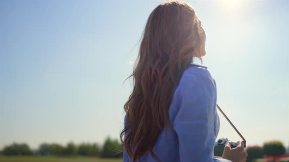 Back View of Unknown Woman with Photo Camera Enjoying Sunlight in Spring Garden alt