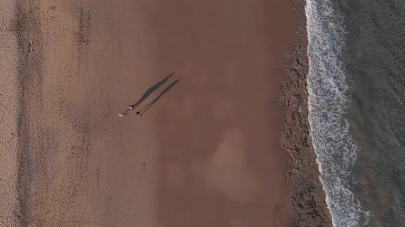 Picturesque summer aerial top down scene of three people walking on sandy Calheta beach by waves rol alt