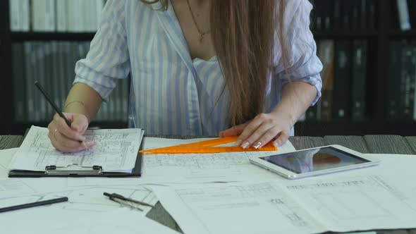 Girl architect sits at a desk and works with drawings close-up