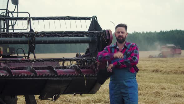 A Tired Farmer Takes Off His Cap and Wipes the Sweat From His Forehead Near the Combine alt