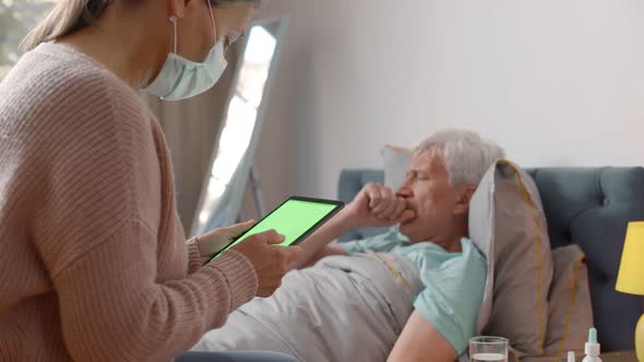 Mature Husband at Home with Flu While Wife in Mask Consulting Doctor Online alt