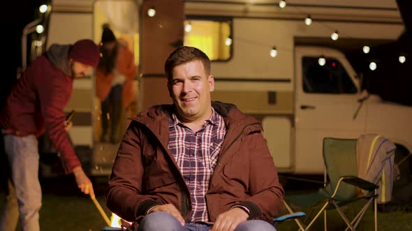 Happy Young Man Sitting on Camping Chair Looking at the Camera alt