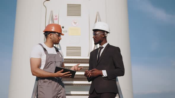 Indian Engineer in Orange Helmet and Grey Overalls Pointing in Distance and alt