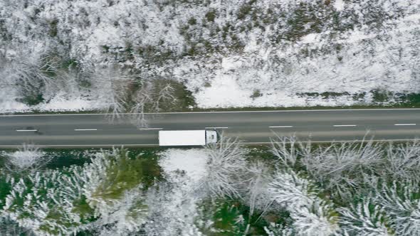 Tracking a lorry from above which is driving along a straight wintry road, framed with trees from a alt