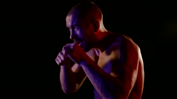 a Muscular Man with a Naked Torso Strikes with His Hands on a Dark Background alt