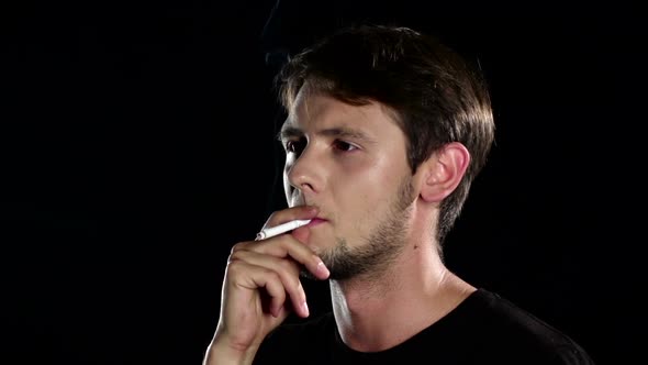 Man Smokes a Cigarette in a Dark Room. Black. Close Up. Slow Motion alt