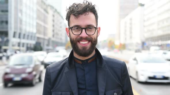 Portrait of young man bearded looking camera smiling wearing glasses alt