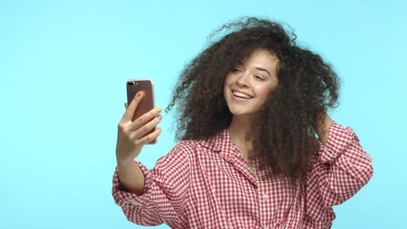 Beautiful Caucasian Woman with Curly Hairstyle Looking at Herself on Smartphone Posing for Selfie