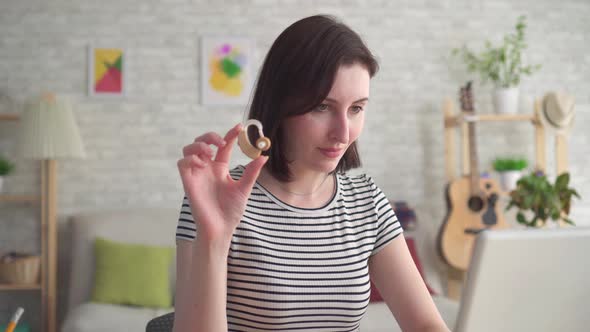Young Woman Looking for Information on the Internet in a Laptop and Holding a Hearing Aid Close Up alt