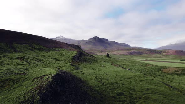 Drone Flight Over Grassy Landscape with Rocks and Mountains alt