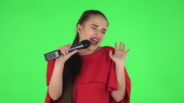 Portrait of Pretty Young Woman Is Singing Into a Microphone and Moving To the Beat of Music. Green alt
