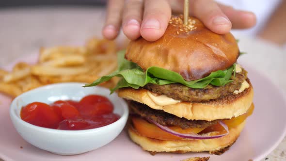 A Hand Fixing a Bun of the Plant Based Double Decker Burger alt
