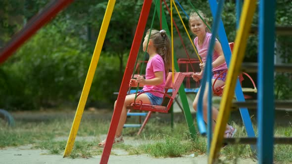 Two girls ride a swing in the Park on a Playground on a summer day.
