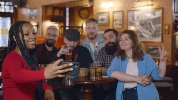 Charming Excited African Woman Taking Selfies with Her Friends at Beer Pub alt