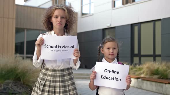 Two Schoolgirls with Placards are Standing in Front of the School Building alt