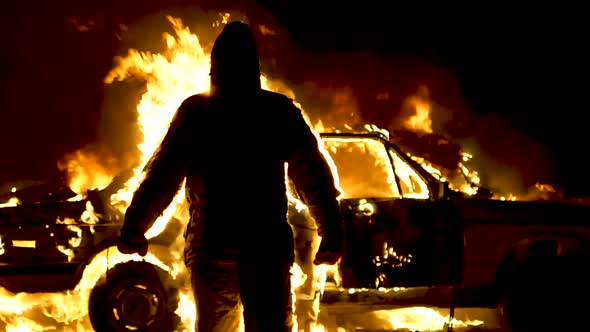 The burning man moves away from the burning car. The man is on fire