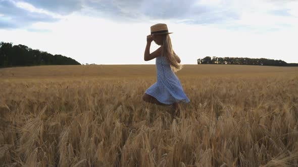 Beautiful Girl with Long Blonde Hair Jogging Over Meadow of Barley at Overcast Day. Cute Happy Child alt
