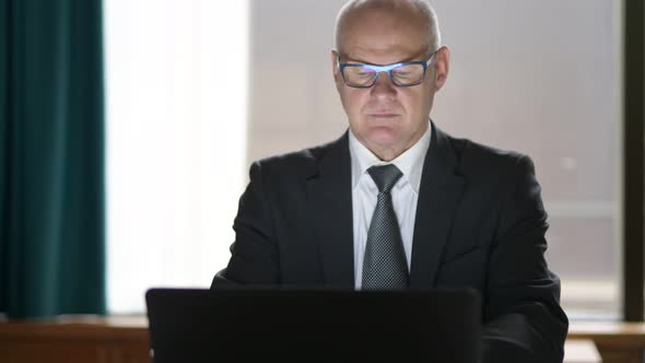 Happy Senior Businessman Using Phone And Laptop While Sitting In The Office alt