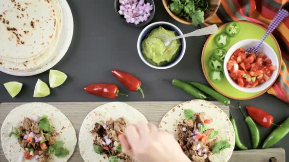 Preparing pulled pork carnitas with pico de gallo on a flour tortilla. alt