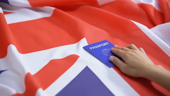 Female Hand Putting International Blue Passport on British Flag, Visa Applicant alt